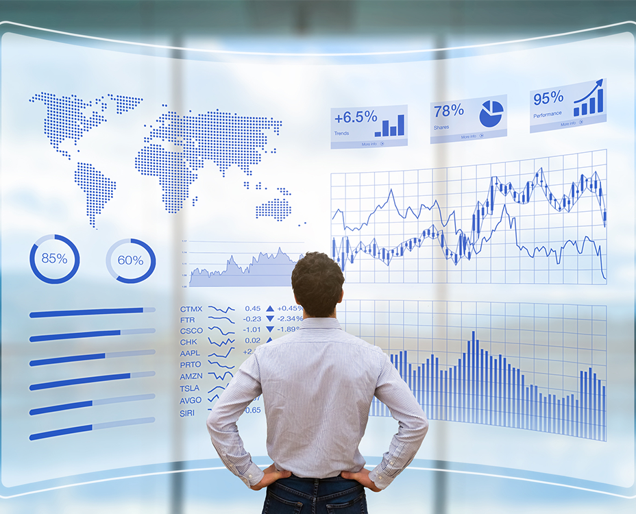 A man in a shirt stands facing a large digital screen displaying global maps, charts, and graphs, indicating data analysis and trends.